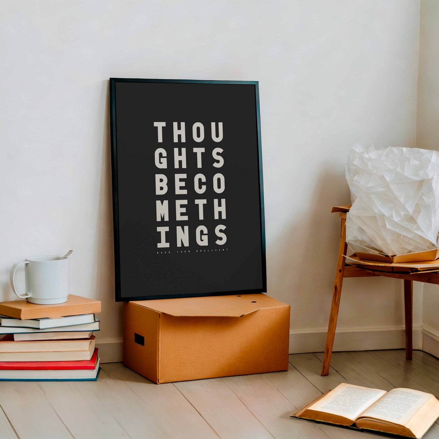 Minimal black and white typography print with the words “Thoughts become things, make them brilliant” displayed in bold type on a neutral wall.