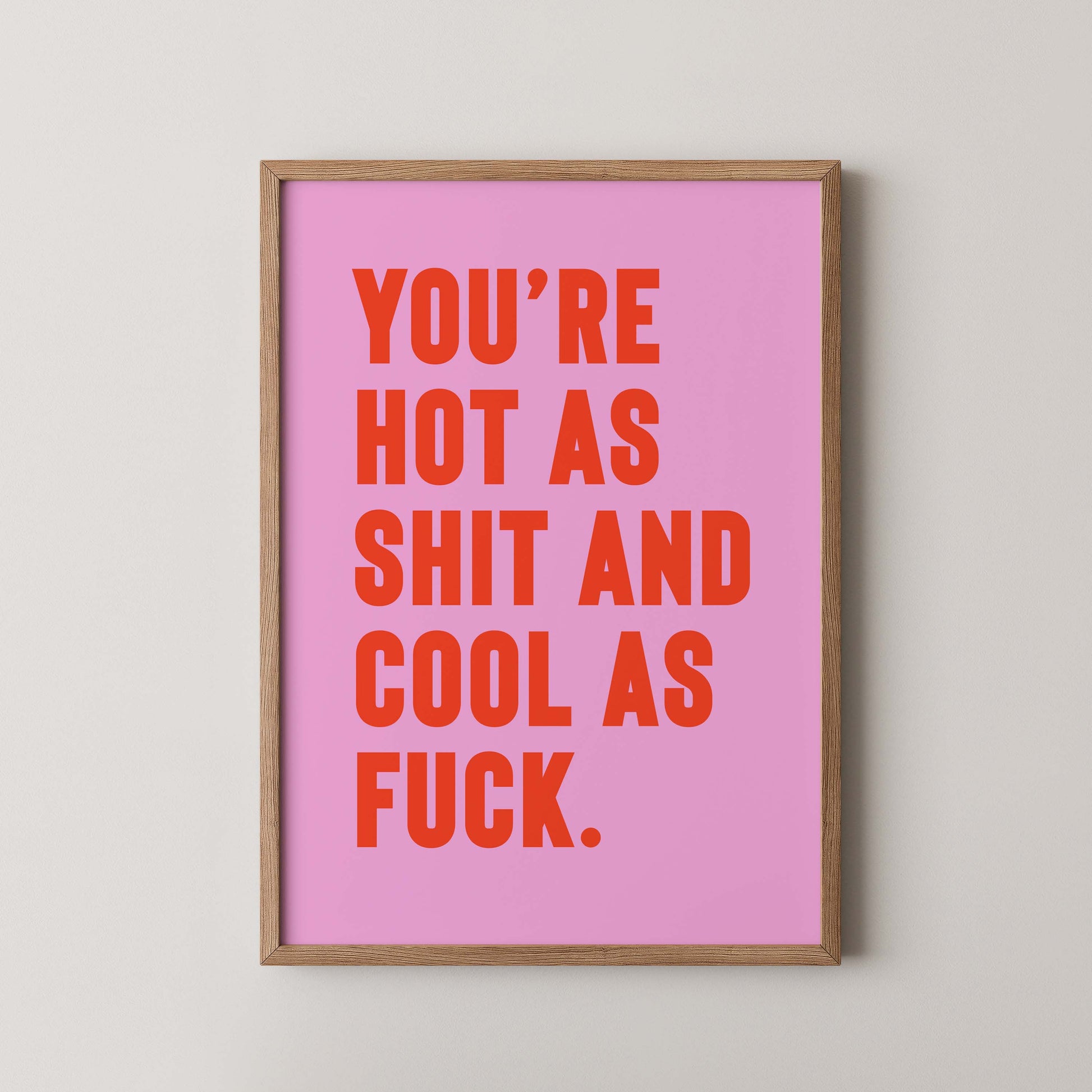 Bold pink and orange typography print that reads “You’re hot as shit and cool as f*ck,” styled in a wooden frame on plain wall.  A cheeky, empowering quote print ideal for renters, couples, or anyone who loves bold graphic art.