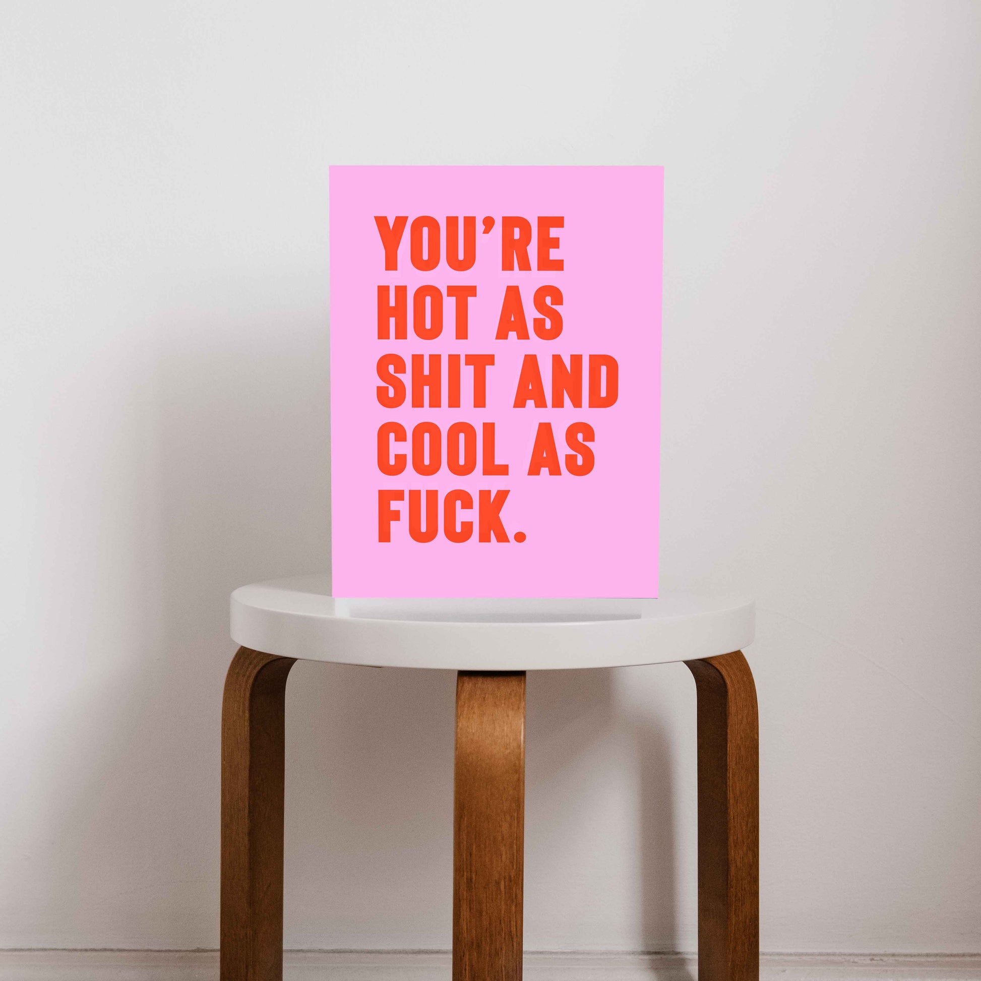 Bold pink and orange typography print that reads “You’re hot as shit and cool as f*ck,” styled on a minimalist stool.  A cheeky, empowering quote print ideal for renters, couples, or anyone who loves bold graphic art.