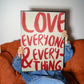 Love Everyone and Everything bold red typography wall art held by person on sofa, modern inspirational quote poster.