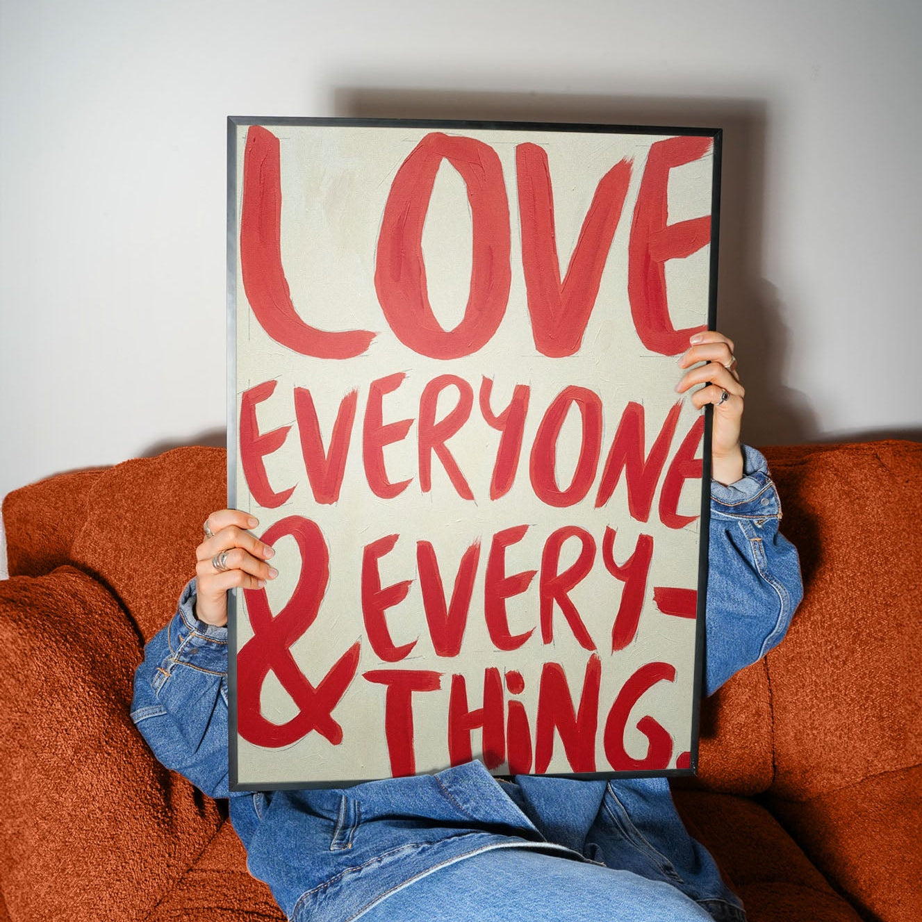 Love Everyone and Everything bold red typography wall art held by person on sofa, modern inspirational quote poster.