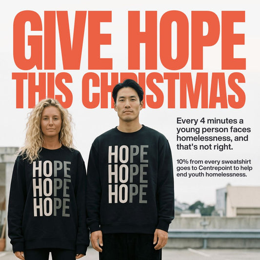 Couple wearing black HOPE sweatshirts, with the text Give Hope This Christmas behind them. 