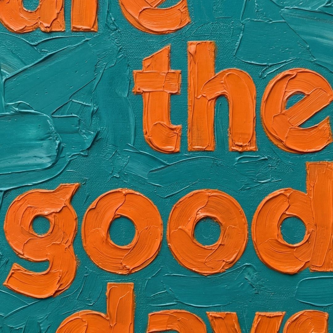 Close-up of textured oil-style typography showing thick brush strokes and layered paint detail in teal and orange. These are the good days quote. 
