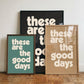 Three framed “These Are The Good Days” typography prints in green, black and neutral beige, styled together against a white wall on a parquet wooden floor.