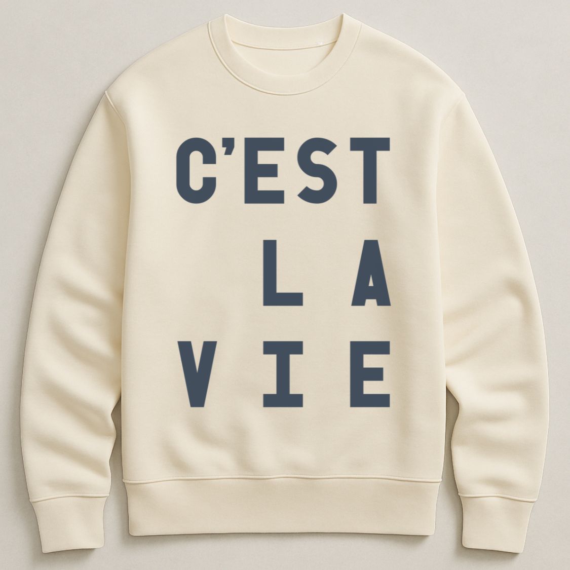 Bold typographic C'est La Vie unisex, oversized sweatshirt, in ivory colour, flay lay photograph on a plain background. 