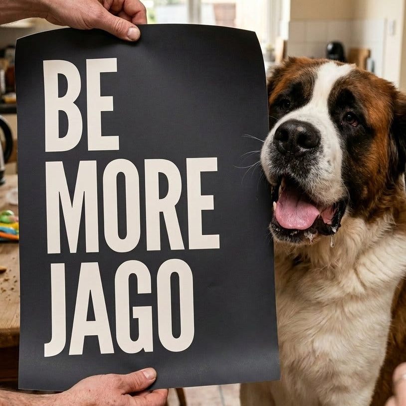 Personalised pet name print reading "Be More Jago" held up next to a Saint Bernard dog in a real family kitchen, custom typographic dog print by Burnt Peach Studio.