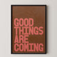 Good Things Are Coming bold typography wall art in coral lettering on a warm brown background, framed modern motivational print.
