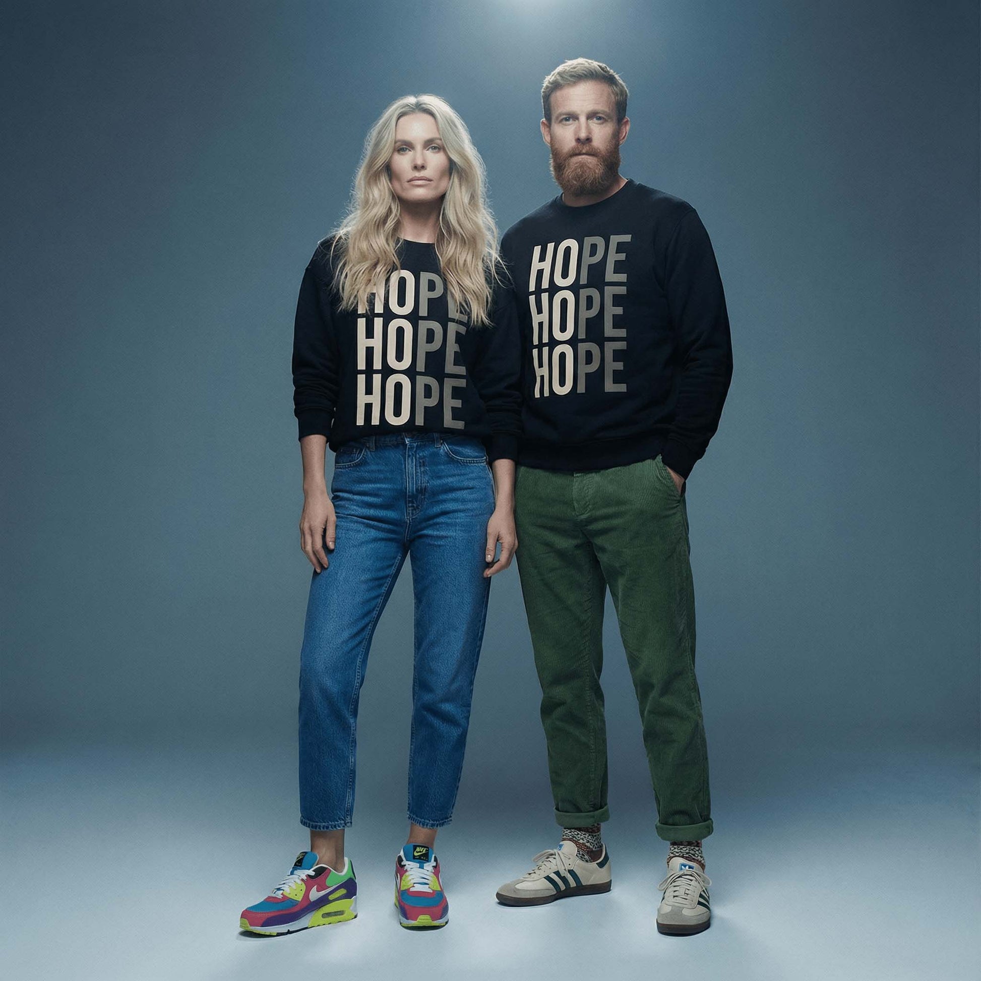 Blonde couple in minimal photostudio, both wearing black Hope sweatshirts, jeans and trainers. 