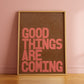 Good Things Are Coming motivational typography print in coral lettering on a warm brown background styled in a contemporary interior.