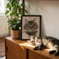 Cat lying on a midcentury sideboard next to custom oil painted portrait of cat framed in black. 