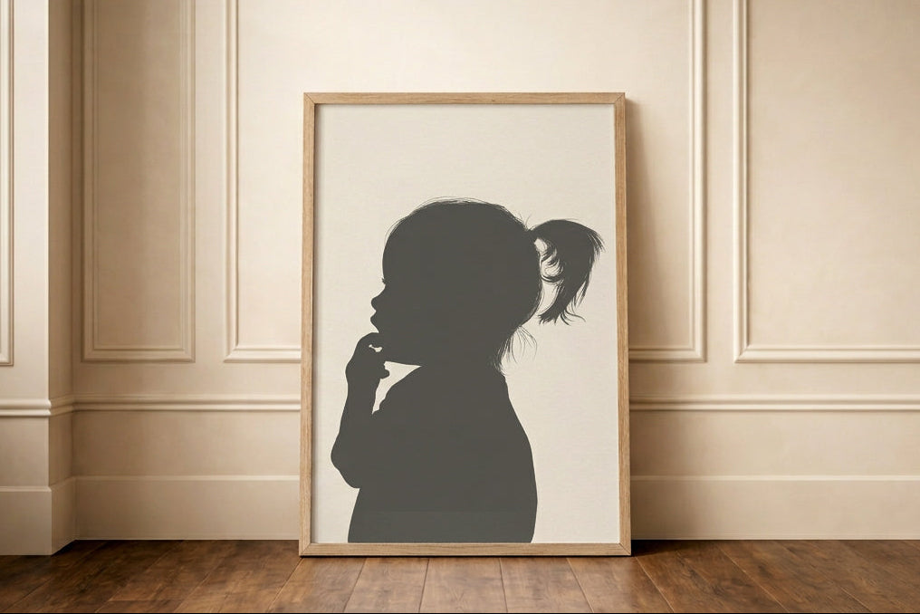 Silhouette portrait of a little girl sucking her fingers, framed in oak, leaning against a cream panelled wall. 