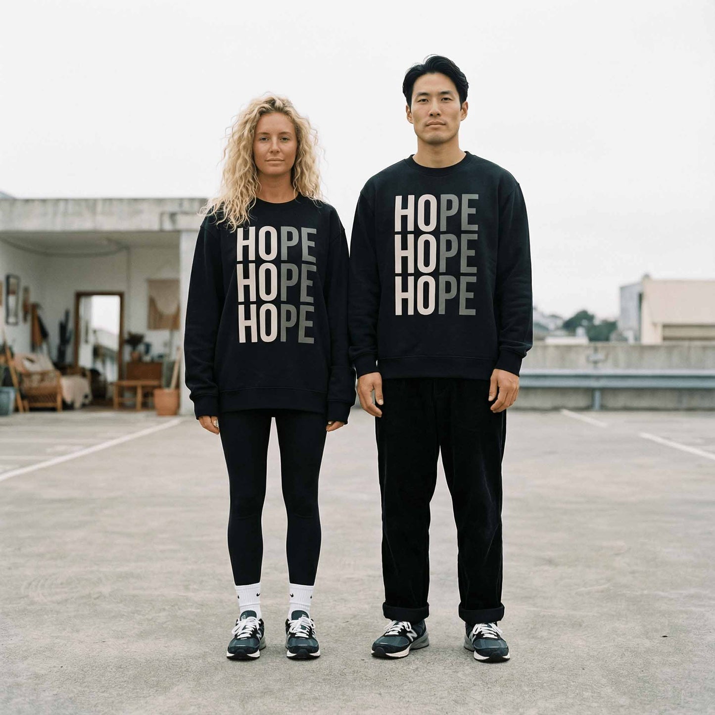Couple wearing black Hope chriarity sweatshirts, standing outside in a parking lot. 