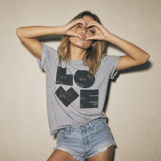 Model wearing grey t-shirt with typographic design LOVE in a vintage style by BurntPeach forming heart shape with her hands. Wearing denim shorts. 