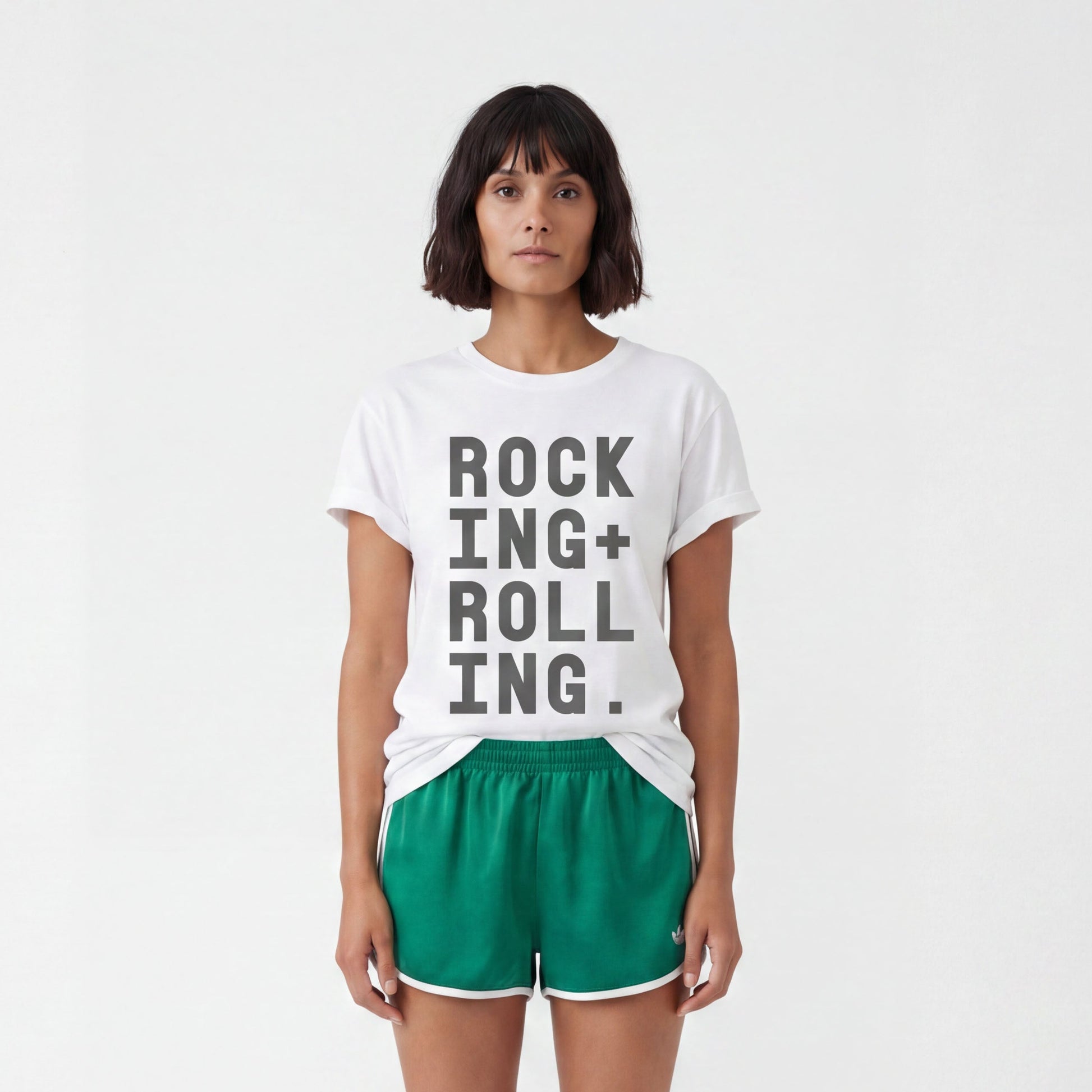 model in white studio wearing a white tshirt with black text Rocking + Rolling styled with green adidas sports shorts. 