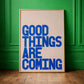 Good Things Are Coming bold blue typography wall art on cream background styled against a green wall interior.