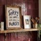 Hangry wall art print, soft oil painted letters in charcoal colour on stone background.  Quote says "I'm sorry for what I said when I was hungry" style in kitchen with burgubdy tiles. 