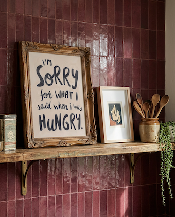 Hangry wall art print, soft oil painted letters in charcoal colour on stone background.  Quote says "I'm sorry for what I said when I was hungry" style in kitchen with burgubdy tiles. 