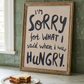 Funny wall art quote next to a half eaten sandwhich.  Hangry wall art print, soft oil painted letters in charcoal colour on stone background.  Quote says "I'm sorry for what I said when I was hungry"