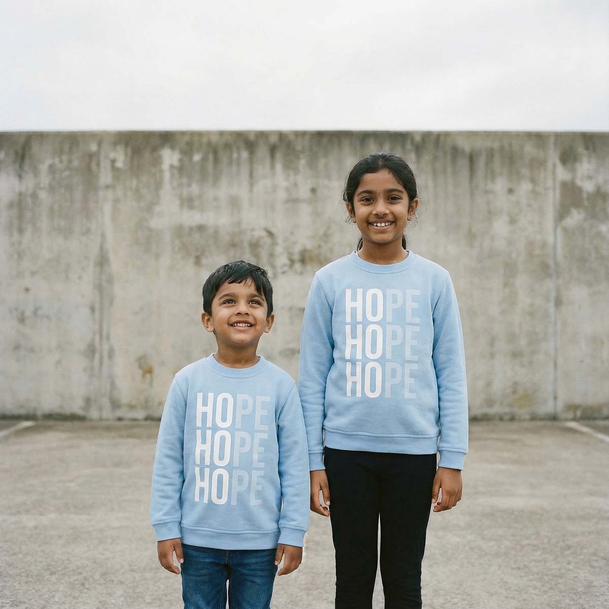 2 children wearing Hope sweatshirt in pale blue with white design. photographed against a concrete wall.  Sweatshirt raising money for Centrepoint charity. 