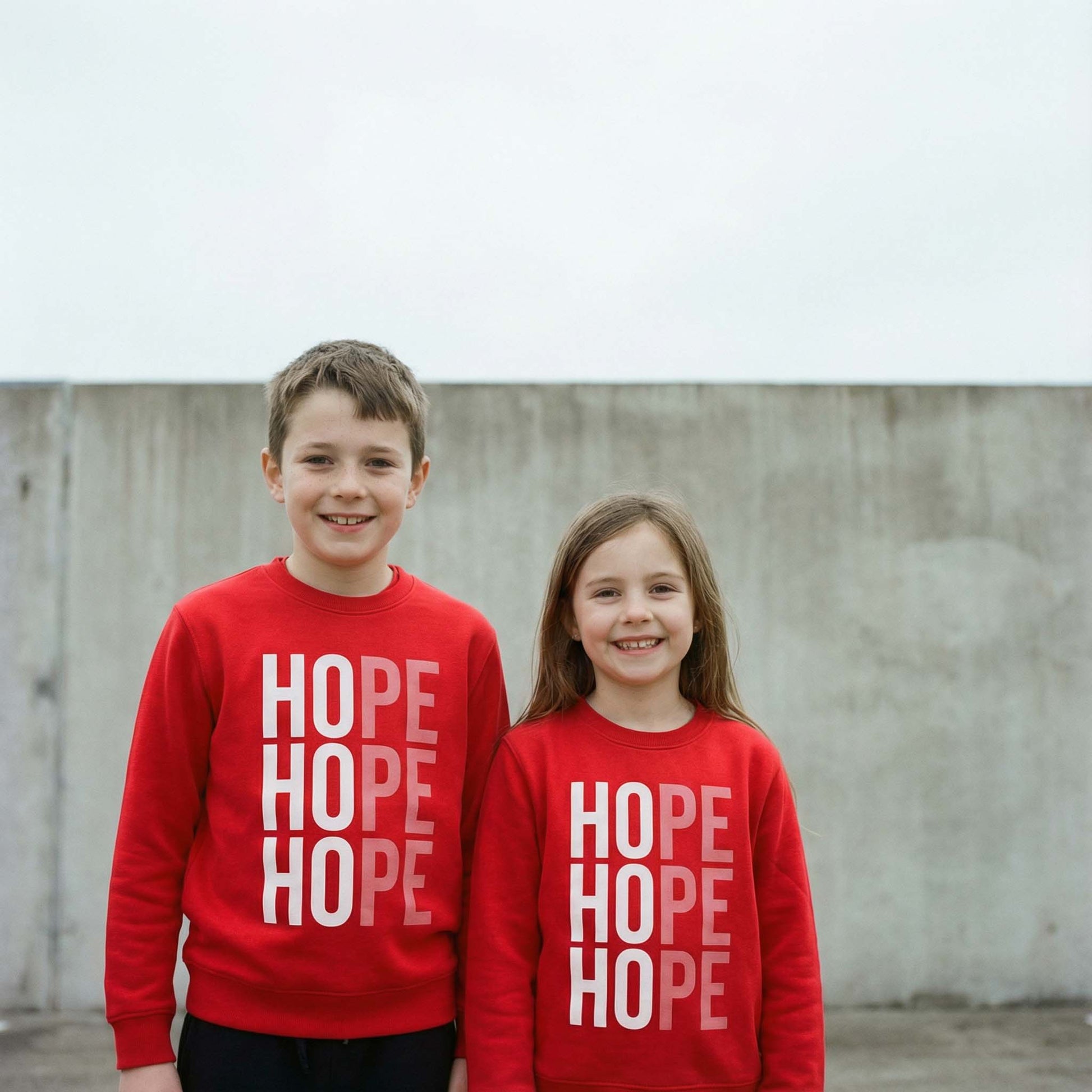 2 children wearing Hope sweatshirt in red with white design. photographed against a concrete wall.  Sweatshirt raising money for Centrepoint charity. 