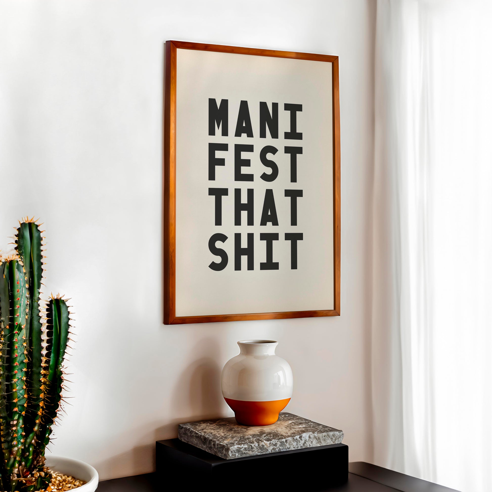 Free printable Manifest That Shit typography wall art in a wooden frame styled on a modern shelf with cactus and neutral home décor.