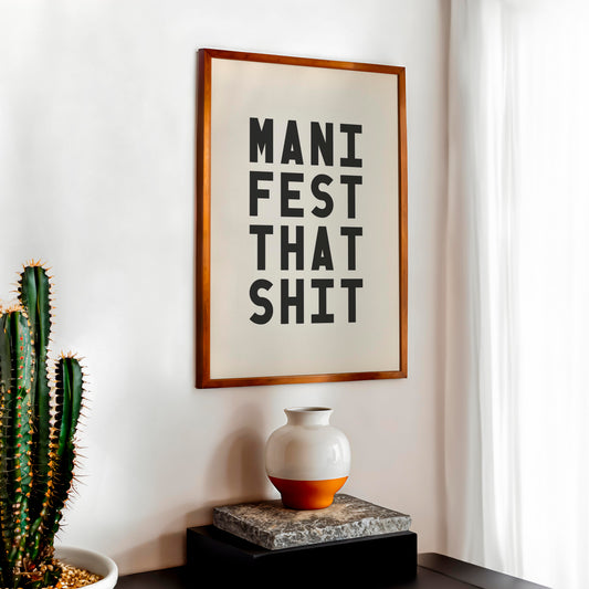Free printable Manifest That Shit typography wall art in a wooden frame styled on a modern shelf with cactus and neutral home décor.
