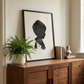 Boys ink silhouette portrait framed in black styled on mid century sideboard next to fern plant. 