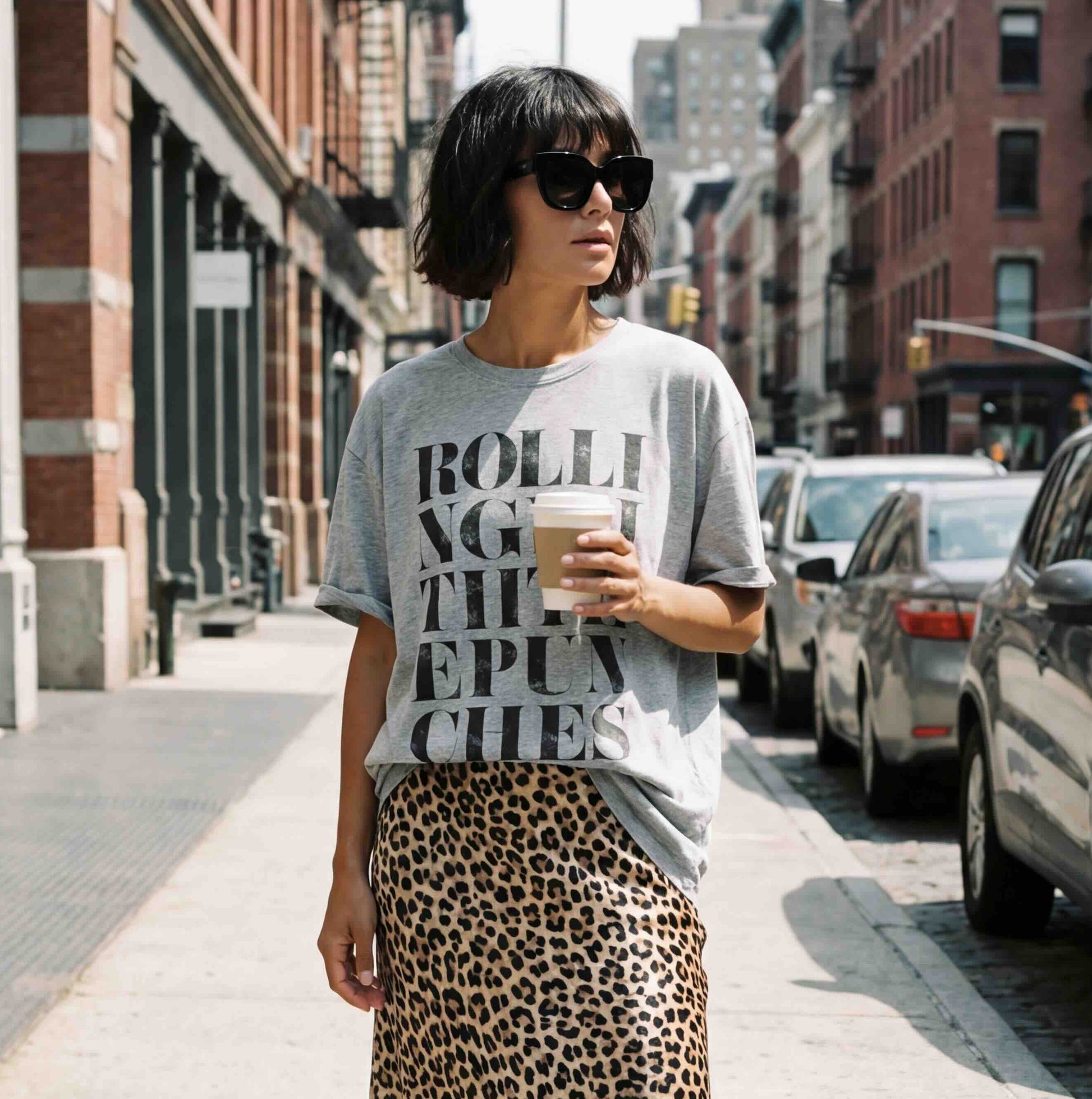 Girl with black bob hair,  in NY street wearing grey Rolling with the punches T-shirt with a leopard print silk skirt, and adidas samba trainers