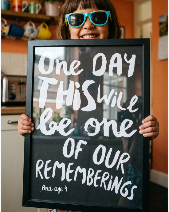 Little girl with sunglasses holding a framed black and white custom made quote print of her quote: One days this will be one of our rememberings