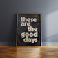 Framed quote print in a painterly oil style, leaning against a wall in an oak frame. Quote is positive and says "These are the good days"