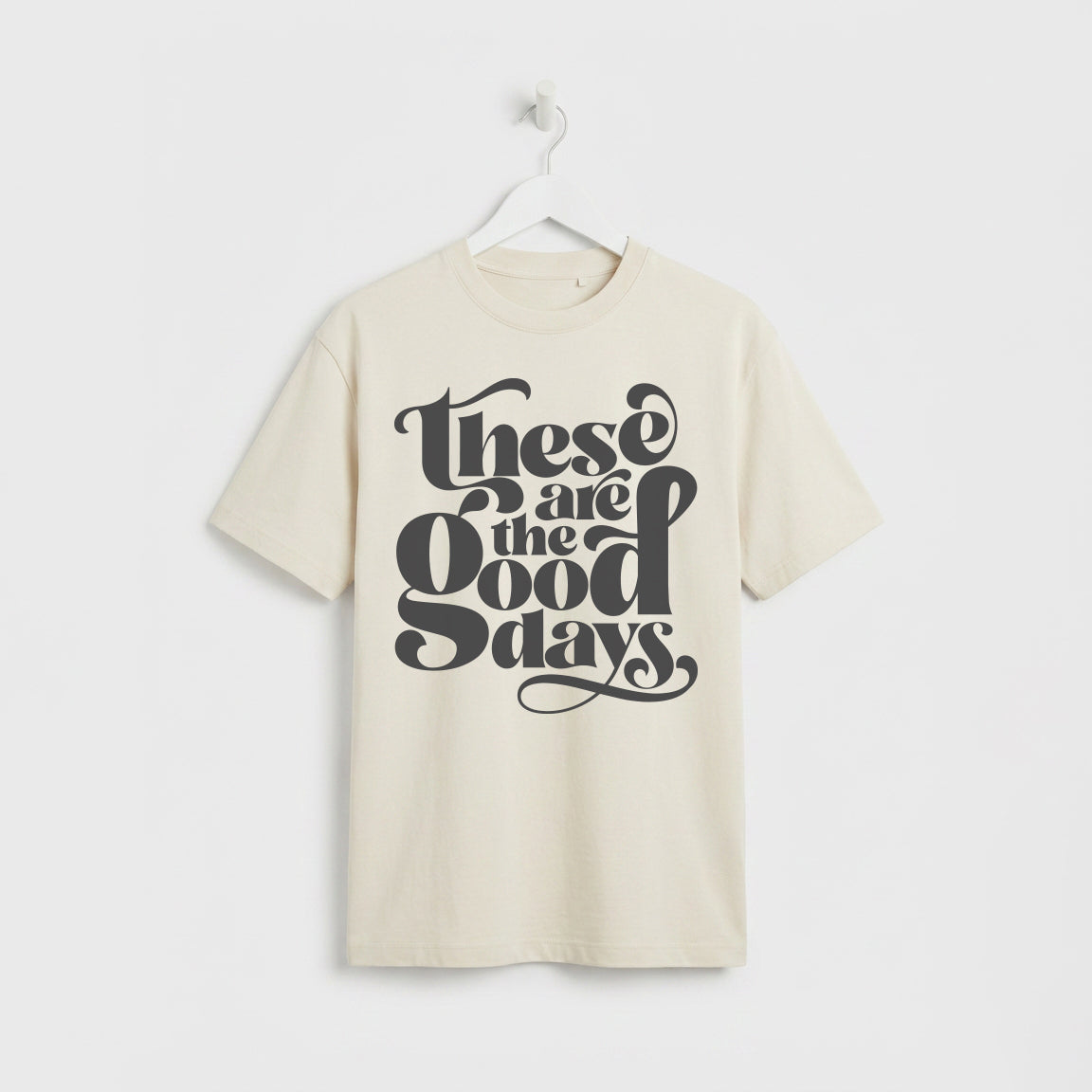 Eco Raw Ecru coloured “These Are the Good Days” graphic t-shirt on white wooden hanger, minimalist studio background