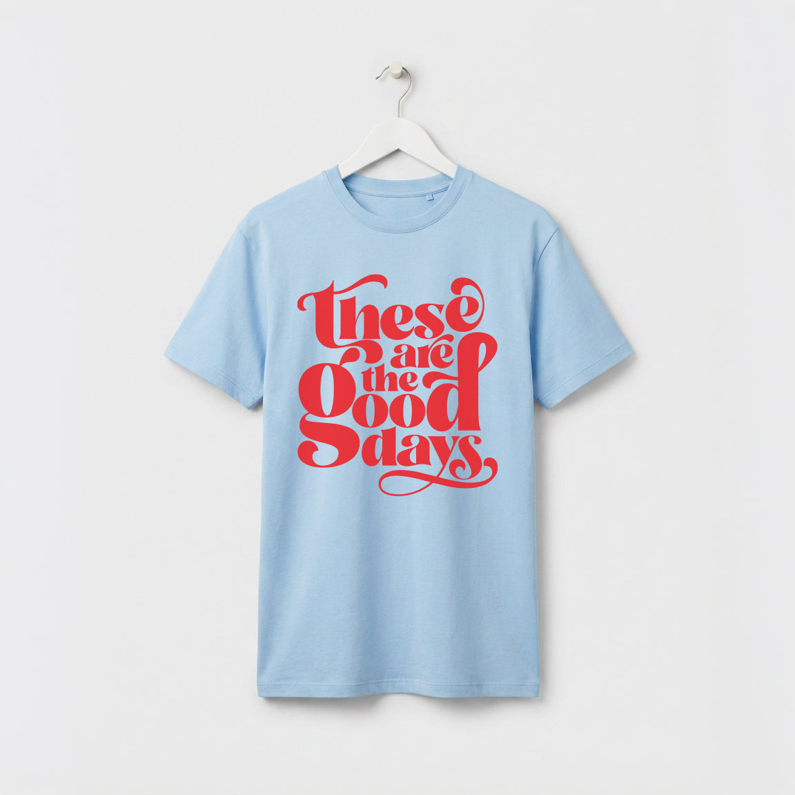 Light Blue and red “These Are the Good Days” graphic t-shirt on white wooden hanger, minimalist studio background