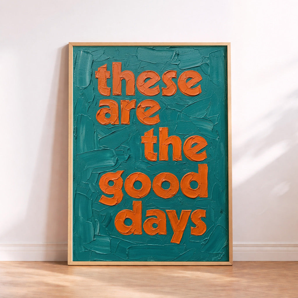 Framed quote print in a painterly oil style, leaning against a wall in an oak frame.  Teal and orange coloured Quote is positive and says "These are the good days"