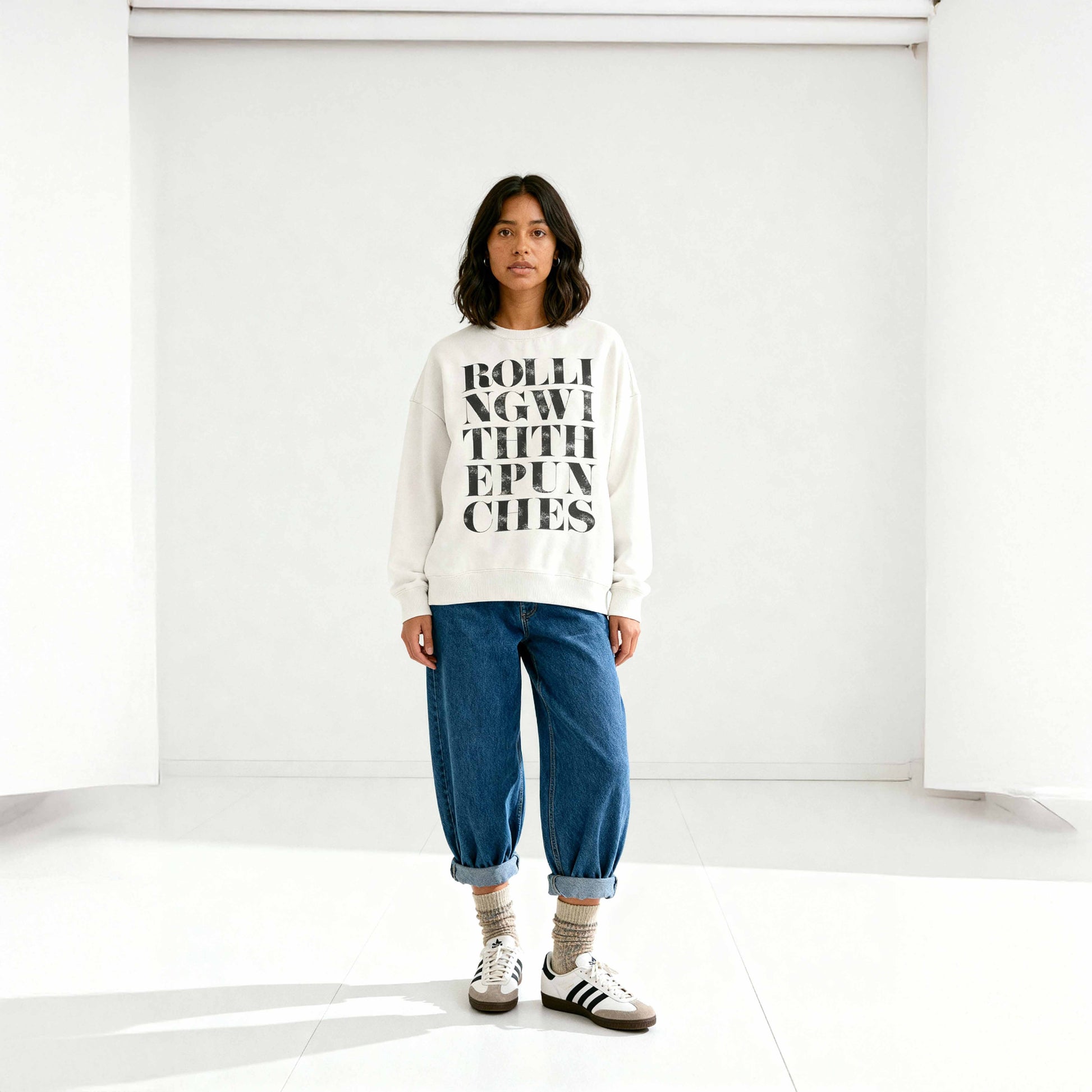 Oversized ivory coloured sweatshirt with Rolling With The Punches typography design styled with jeans on latina model in minimalist studio. 