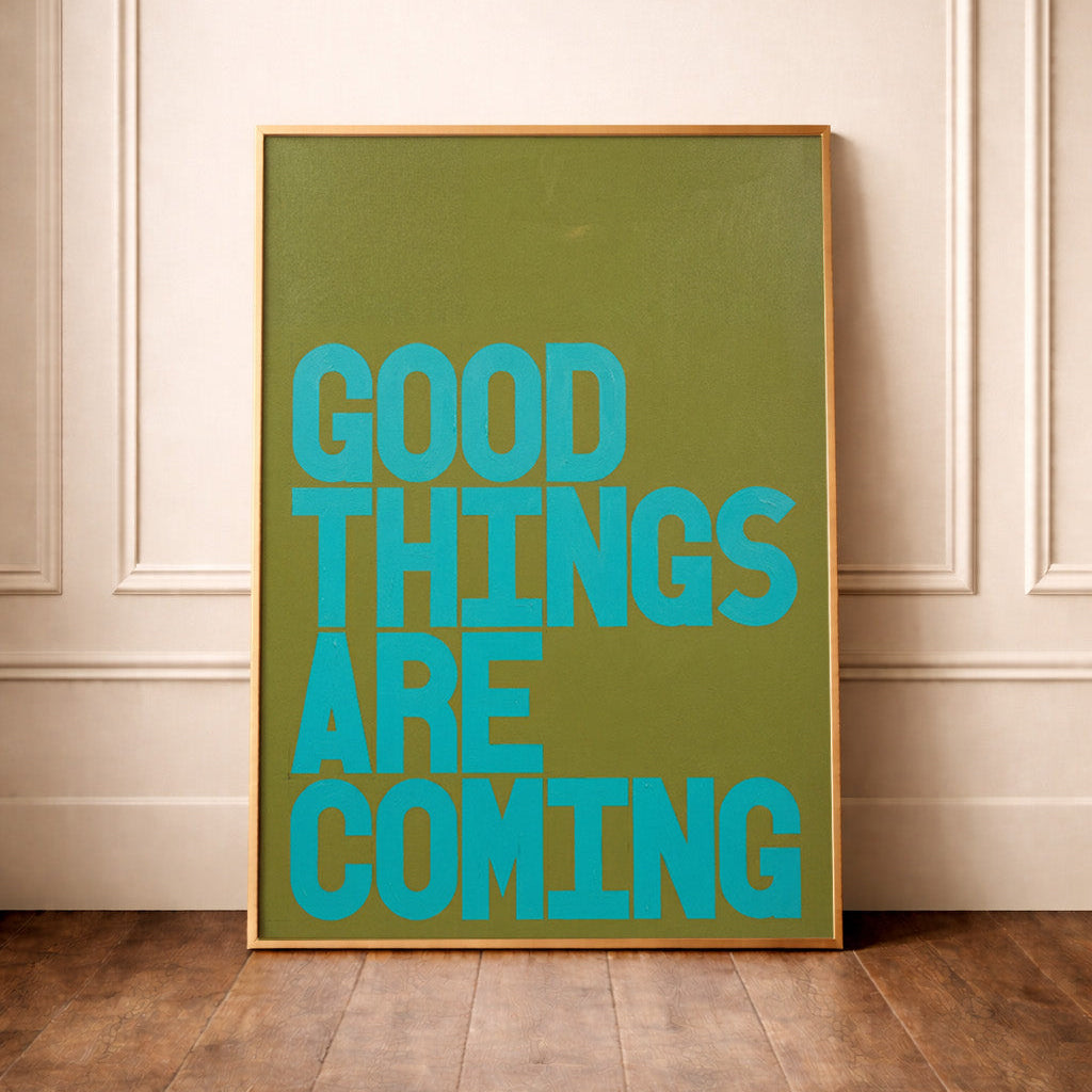 Good Things Are Coming turquoise typography poster on green background styled leaning against a wall in a neutral interior.