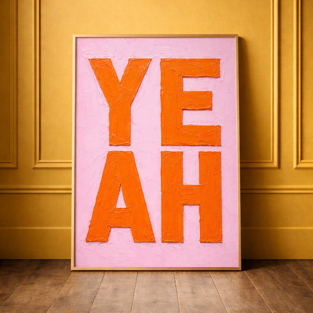 bright pink and orange painted oil painting bold typography print saying YEAH framed in brass leaning against a yellow wall. 