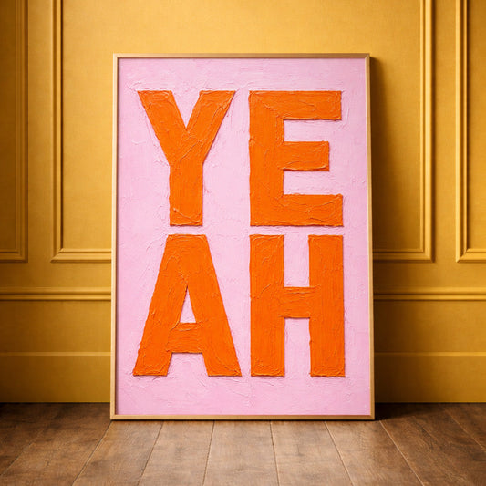 bright pink and orange painted oil painting bold typography print saying YEAH framed in brass leaning against a yellow wall. 