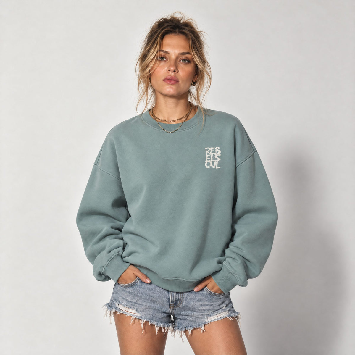 Woman wearing the Rebel Soul organic sweatshirt in jade with denim shorts, by Burnt Peach
